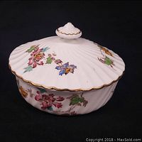 Side view of the covered container showing floral gilt decoration and scalloped gilt edged lid with knob.