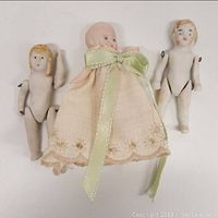 Three antique bisque jointed dolls; two nude and one dressed in embroidered dress with bow