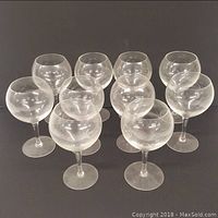 Ten clear round wine glasses arranged in two rows on black background