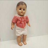 Full front view of antique composition doll standing, wearing red and white striped shirt and white shorts, showing molded hair and painted face.