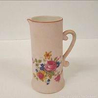 Front view of bisque porcelain pitcher showing detailed floral decoration and pink tint.