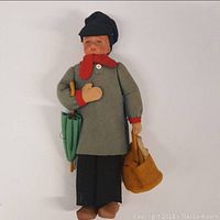 Full view of doll wearing gray felt coat, red scarf, black pants and cap, holding umbrella and bag