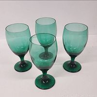 Four green hand blown wine glasses arranged in a group against a neutral background, showing their size, shape, and color.