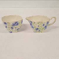 Front view of sugar bowl and creamer showing chintz pattern with blue flowers and green foliage