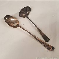 Photo showing two silver plated serving utensils, a large serving spoon and a ladle, with visible tarnish and wear.