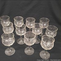 Set of twelve crystal stemware wine glasses arranged on black background. Each glass has etched floral designs on the bowl and faceted decorative stems.