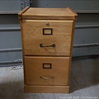 Front view of the oak file cabinet showing its two drawers closed, metal handles, label holders, and keyhole lock on the top drawer.