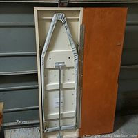 Open cabinet reveals fold-out ironing board with padded cover and metal support system.