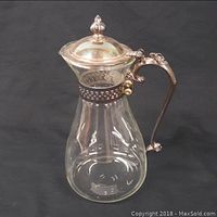 Full view of the glass carafe pitcher showing the clear glass body with silverplate handle, lid, and collar.