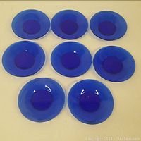 Top view of all 8 cobalt blue glass plates arranged on a flat surface.