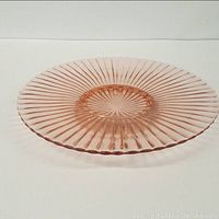 Side angled view of large pink Depression glass pedestal charger, showing ribbed pattern and pedestal base.