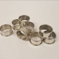 Group of nine plain pewter napkin rings showing smooth cylindrical shape with slightly flared edges.