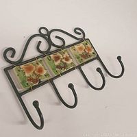 Front angled view showing four hooks and three glazed floral tiles on black metal hanger