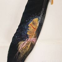 Close-up of the black feather showing the detailed painted Native American portrait in profile with colored facial markings and scarf.