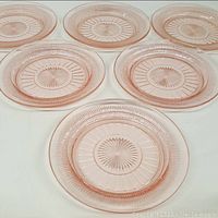 Six pink Depression glass small plates arranged flat showing the sunburst and ridged pattern clearly on each plate, viewed from above.