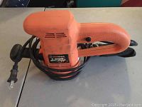 Orange Black and Decker sander laying flat on a table showing side profile and power cord