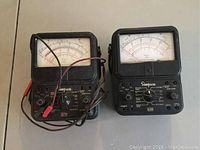 Two vintage analog voltage meters side by side, model 260 on right and model 270 on left, both with black casing and large measurement dials, with one set of wires attached.