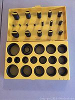 View of the yellow plastic case open showing various sizes of black rubber O-rings in molded compartments, mostly full.