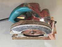 Side view of Makita circular saw showing paint on body, rusty circular blade, and worn metal base.