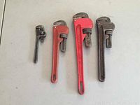 Four crescent pipe wrenches laid on a flat surface showing varying sizes and finishes, one large red made in Taiwan.