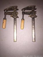 Photo showing two metal bar clamps with wood handles laying side by side from above.