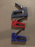 Top view of three staple guns: large black Swing Line, medium red Arrow, small blue LittleShooter arranged in descending size order.