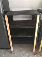 Front view of wood rolling shelving unit showing four wooden slatted shelves with metal frame and casters. Shelves show wear marks.