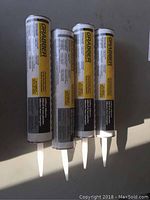 Four tubes of Grabber brand subfloor adhesive arranged upright, showing label and nozzle tips.