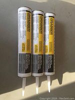 Front view of three tubes of Grabber Subfloor Adhesive with yellow and black labeling showing brand and product details.