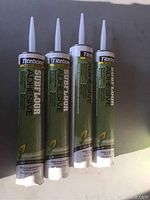 Four tubes of Titebond Subfloor Adhesive standing upright on a flat surface, showing front labels and nozzles.