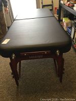 Full-length view of the open massage table showing black vinyl top and wooden legs