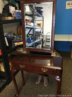 Queen Anne style hall table with curved legs, glass top and brass drawer pulls paired with Bombay Company mirror reflecting surroundings.