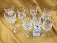 Six tall Cristal d'Arques Longchamp Gold rimmed crystal wine glasses and two additional crystal wine glasses arranged on mustard yellow fabric, displaying all eight glasses and their cut patterns.