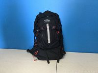 Front view of large black backpack with multiple straps and attachment loops against blue background