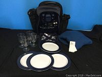 Picnic backpack displayed with four plates, four wine glasses, cutlery, and salt and pepper shakers.