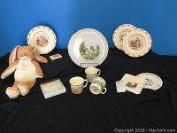 Full lot front view showing plates, mugs, stuffed toy, and notepad on black background.