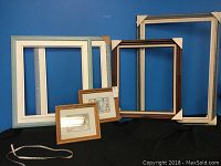 Collection of six assorted picture frames displayed against a blue backdrop, including four large empty frames and two smaller framed artworks.