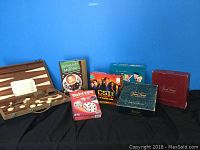 Overall view of seven game sets including a wooden backgammon set with white pieces and six boxed board games.