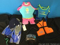 Photo showing three flotation vests, Disney children's swimwear, blue flippers, goggles, swim hat, and snorkel on a black background.