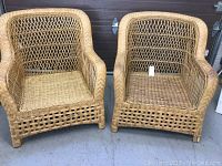 Two natural wicker armchairs displayed side by side on a concrete floor, showing overall design and condition.