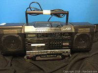 Front view of JVC portable CD and cassette stereo system boom box with attached detachable speakers, control buttons, display, and wired handle.