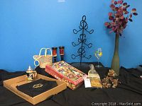 The full collection of wine accessories and related items arranged on a black cloth against a blue wall. Items include wire wine holders, pottery glasses, a box of puzzle, vase, apron, grape clusters, a cheeseboard and a basket.