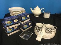 Full lot showing white ironstone plates stacked, white teapot, six boxes of Kerrigan tea pods, clear square dish, two black and white mugs on white tray.