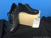 Pair of black leather Ecco women's walking shoes on beige box against blue background
