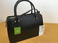 Front view of black leather Kate Spade satchel with gold-tone hardware and green swing tag