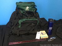 Front view of the hiking knapsack, water bottle, and knife sets with a ruler in front for scale.