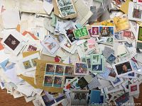 Close-up view of loose Canadian stamps, showing variety of designs, colors, and some attached paper from envelopes.