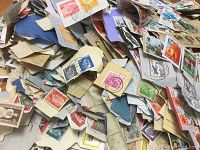 Photo showing a bulk pile of various international postage stamps, many still attached to pieces of envelopes or paper with visible cancellations and postmarks.