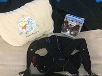 Photo showing Baby Bjorn snuggly baby carrier in black with blue trim along with new Robeez brown leather baby shoes in original packaging.