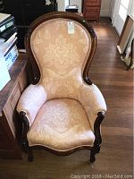 Front view of Victorian armchair showing carved wooden frame and patterned upholstery with floral damask design.